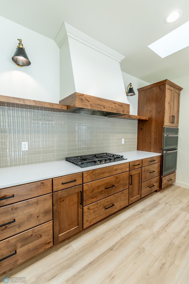 662 Rania Way W, West Fargo, ND 58078 - kitchen with stainless steel appliances, a skylight, light wood finished floors, brown cabinets, and premium range hood