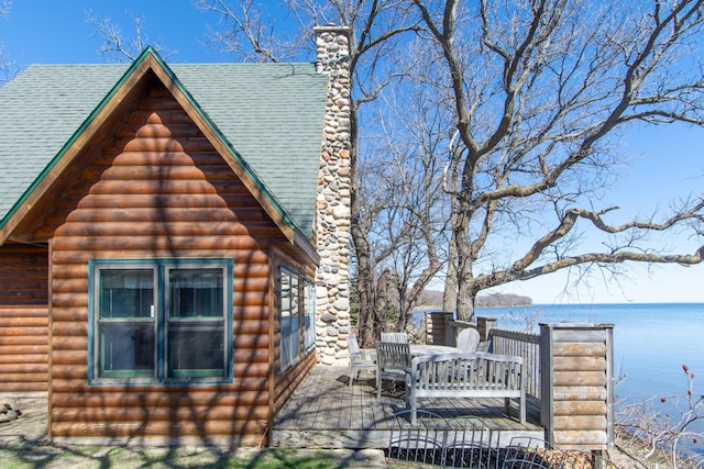 view of property exterior with a deck with water view, roof with shingles, a chimney, and log veneer siding