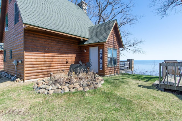 view of home's exterior with a deck with water view, log veneer siding, roof with shingles, a chimney, and a lawn