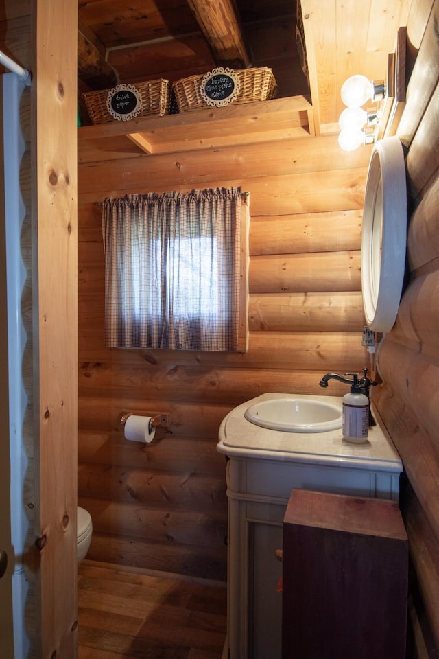 half bathroom featuring wood finished floors, vanity, beamed ceiling, rustic walls, and toilet