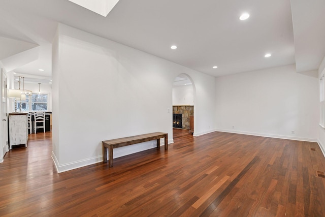 18975 Highland Ave, Deephaven, MN 55391 - unfurnished living room with dark wood-style flooring, a stone fireplace, recessed lighting, baseboards, and a skylight
