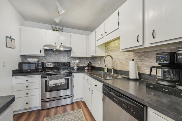kitchen featuring dark wood-style flooring, dark countertops, a sink, appliances with stainless steel finishes, and under cabinet range hood