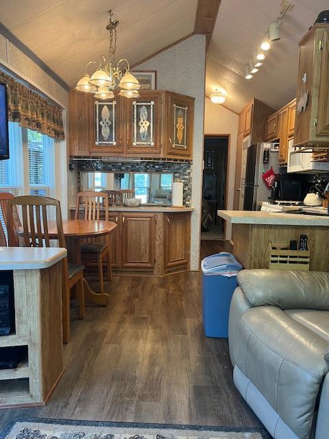 kitchen featuring dark wood-style flooring, a chandelier, brown cabinets, vaulted ceiling, and freestanding refrigerator