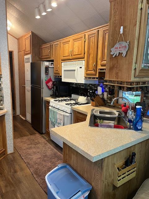 kitchen with light countertops, vaulted ceiling, white appliances, a sink, and wood finished floors