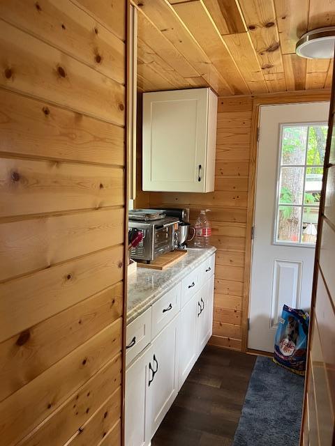 kitchen with white cabinets, dark wood-style flooring, wood ceiling, and wood walls