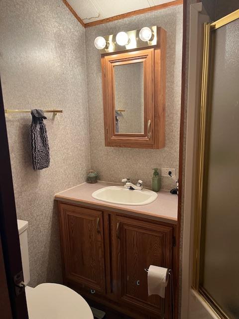 bathroom with toilet, vanity, a shower with door, and wallpapered walls