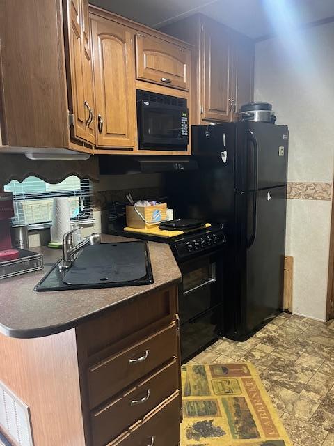 kitchen with dark countertops, black appliances, stone finish flooring, and a sink