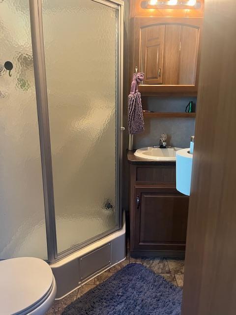 bathroom featuring toilet, a shower with shower door, and vanity