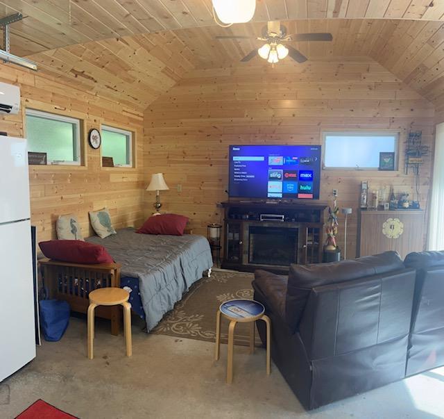 bedroom with wooden ceiling, freestanding refrigerator, multiple windows, wooden walls, and lofted ceiling