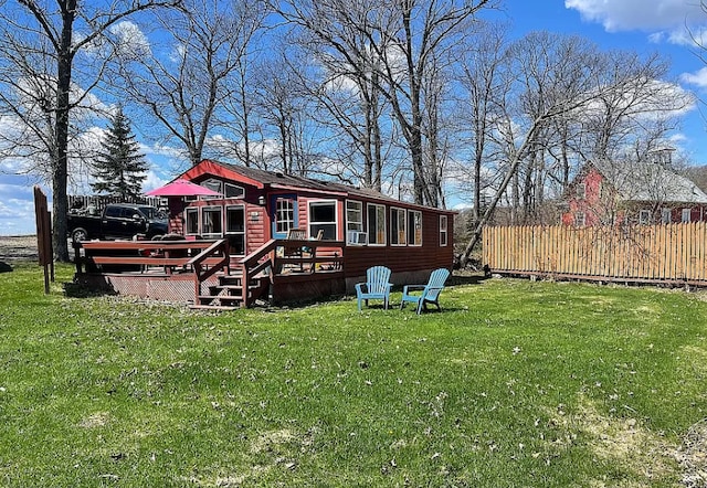 rear view of property featuring a wooden deck, a yard, and fence