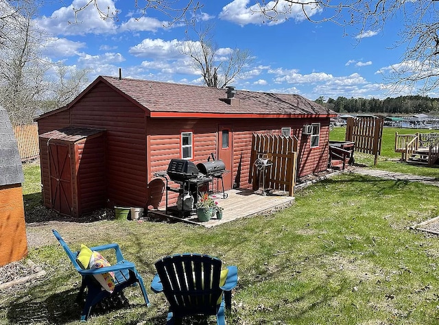 rear view of property featuring an outbuilding, a storage unit, a lawn, and roof with shingles