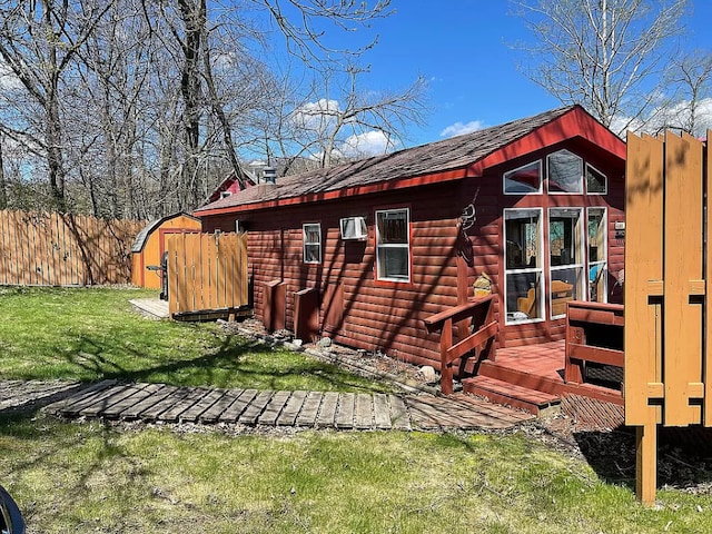 back of property with fence, roof with shingles, a storage shed, a yard, and an outbuilding