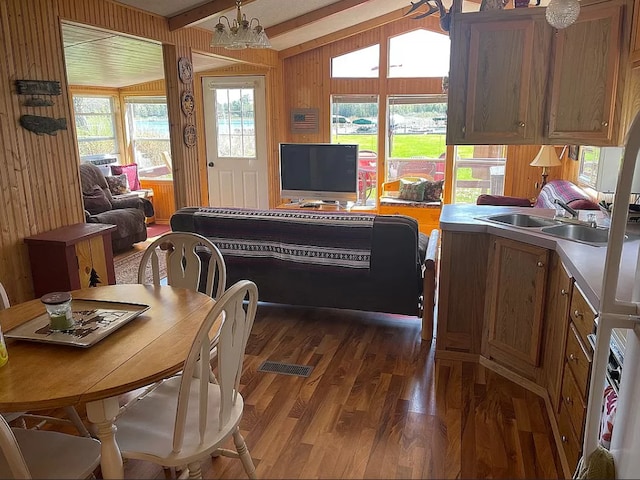 dining space with dark wood-type flooring, wooden walls, an inviting chandelier, and vaulted ceiling with beams