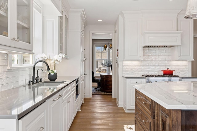 kitchen with a sink, backsplash, light wood-type flooring, and white cabinetry