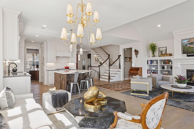 living area with an inviting chandelier, a glass covered fireplace, wood finished floors, and stairway