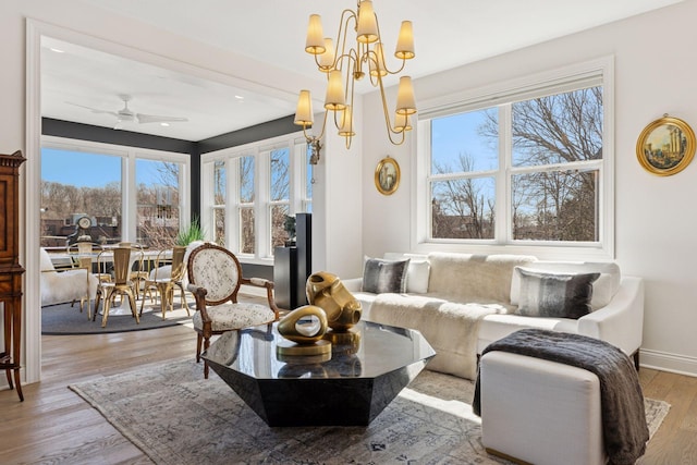 living area featuring baseboards, light wood-style flooring, and ceiling fan with notable chandelier