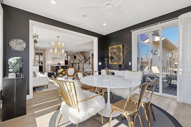 dining space featuring light wood-style floors, recessed lighting, stairs, and ceiling fan with notable chandelier