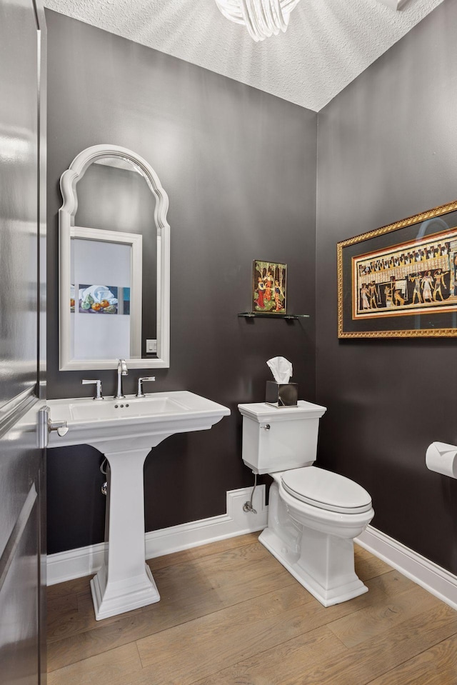 bathroom featuring baseboards, wood finished floors, and toilet