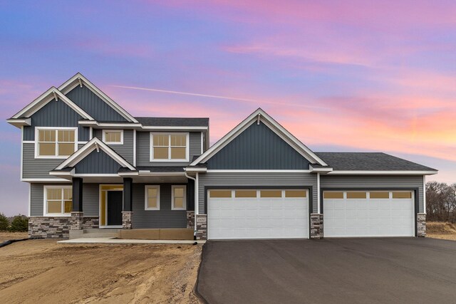 craftsman inspired home featuring aphalt driveway, an attached garage, and stone siding