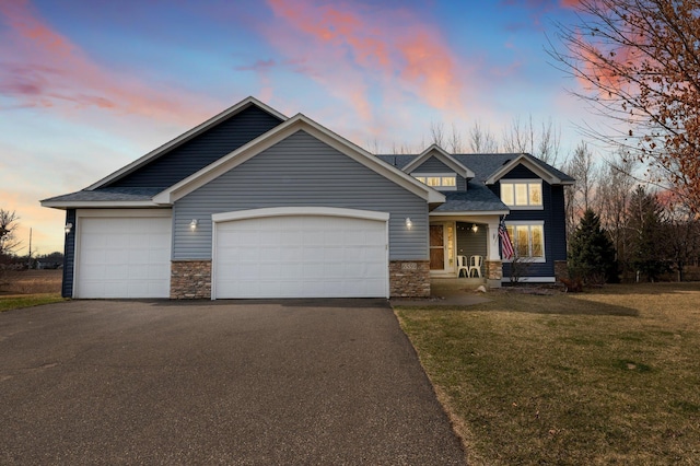 craftsman house featuring driveway, stone siding, a shingled roof, an attached garage, and a yard