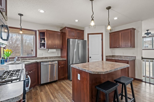 kitchen featuring decorative light fixtures, a center island, a sink, dark wood-style floors, and stainless steel appliances