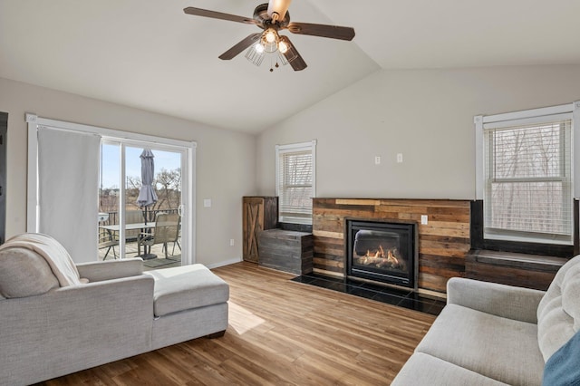 living area with ceiling fan, baseboards, a fireplace with flush hearth, wood finished floors, and vaulted ceiling