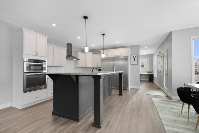 5204 Porchlight, Woodbury, MN 55129 - kitchen featuring stainless steel appliances, white cabinets, light wood-style floors, a kitchen breakfast bar, and wall chimney exhaust hood