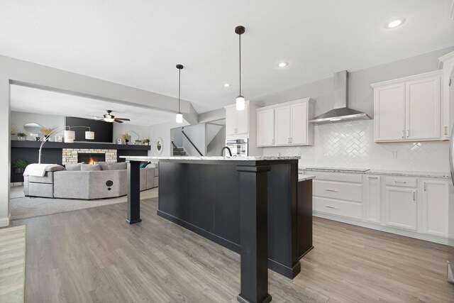 5204 Porchlight, Woodbury, MN 55129 - kitchen featuring light wood-style flooring, tasteful backsplash, a warm lit fireplace, white cabinets, and wall chimney range hood