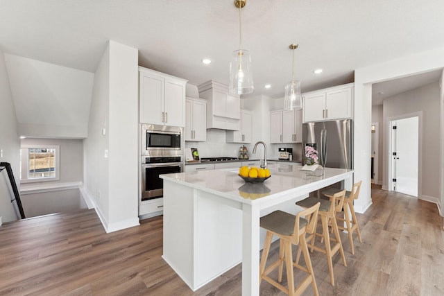 10071 Arrowwood Trl, Woodbury, MN 55129 - kitchen with stainless steel appliances, light wood finished floors, a kitchen island with sink, a breakfast bar, and decorative backsplash