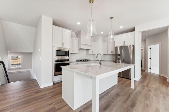 10071 Arrowwood Trl, Woodbury, MN 55129 - kitchen featuring stainless steel appliances, tasteful backsplash, an island with sink, light stone counters, and light wood finished floors