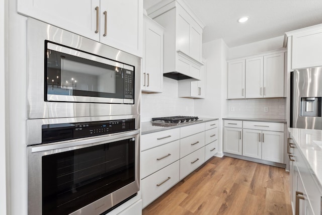 10071 Arrowwood Trl, Woodbury, MN 55129 - kitchen with stainless steel appliances, light countertops, white cabinets, light wood finished floors, and backsplash