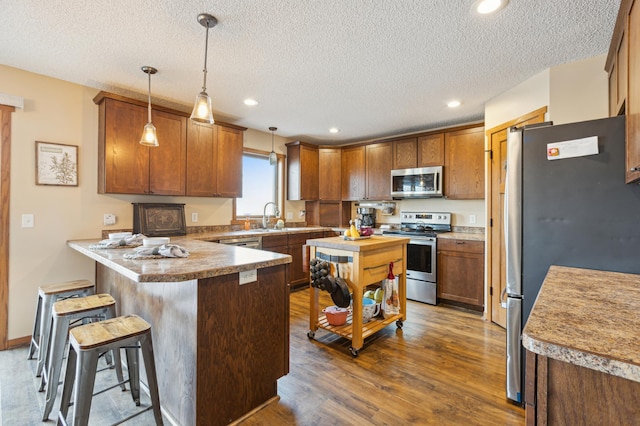 kitchen featuring pendant lighting, a sink, dark wood finished floors, stainless steel appliances, and a peninsula