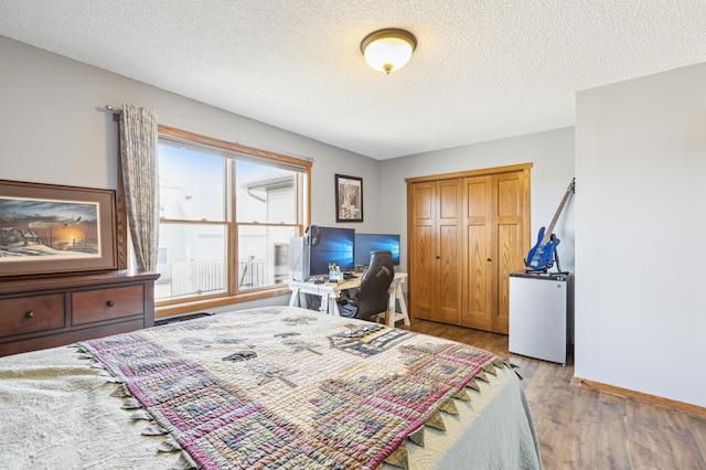 bedroom with a textured ceiling, fridge, a closet, light wood finished floors, and baseboards