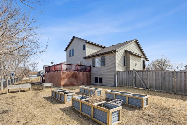 back of property with a gate, a wooden deck, a vegetable garden, and fence