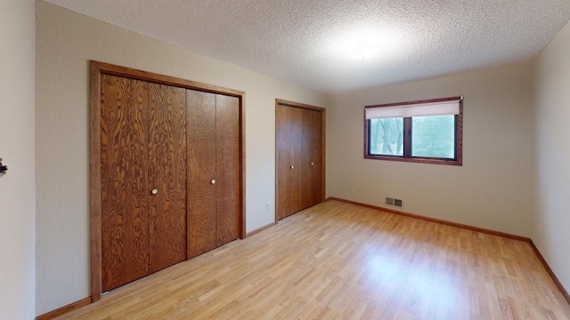 2342 75th Ave, Princeton, MN 55371 - unfurnished bedroom with multiple closets, light wood-style floors, a textured ceiling, and baseboards