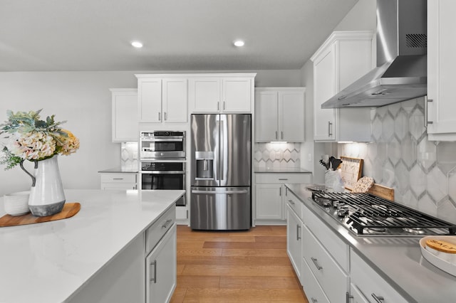 kitchen featuring white cabinets, wall chimney exhaust hood, light wood-type flooring, and appliances with stainless steel finishes