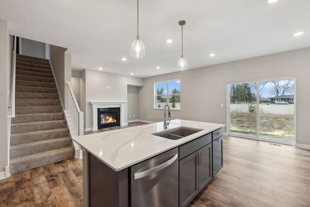 kitchen featuring stainless steel dishwasher, a sink, a glass covered fireplace, wood finished floors, and hanging light fixtures