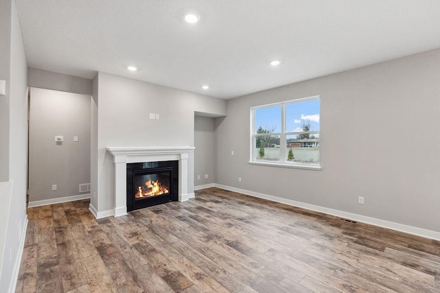 unfurnished living room featuring wood finished floors, a glass covered fireplace, recessed lighting, and baseboards