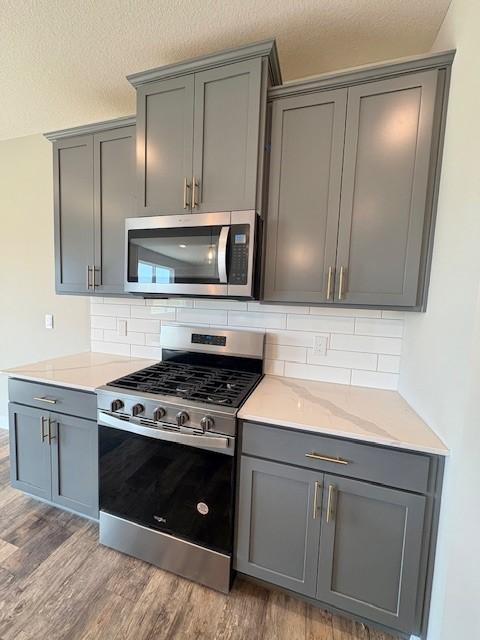 6187 Jensen Alcove S, Cottage Grove, MN 55016 - kitchen with stainless steel appliances, gray cabinetry, light wood-type flooring, decorative backsplash, and a textured ceiling