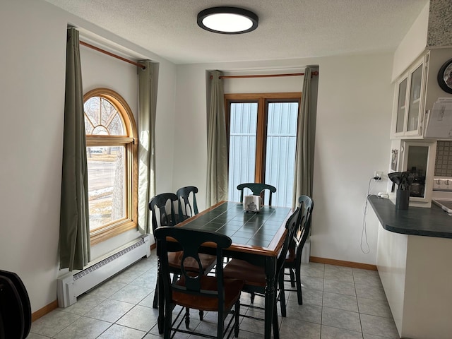 dining room featuring baseboards, a textured ceiling, light tile patterned floors, and a baseboard heating unit
