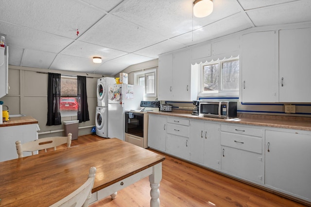 kitchen with light wood-style flooring, stainless steel microwave, vaulted ceiling, electric range oven, and stacked washing maching and dryer
