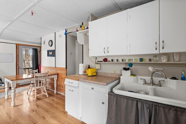 kitchen with open shelves, light wood-style floors, light countertops, a sink, and white cabinetry
