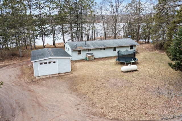 exterior space with a trampoline, a storage unit, an outbuilding, a garage, and dirt driveway