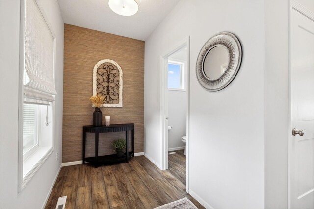 hall featuring dark wood finished floors, baseboards, visible vents, and an accent wall