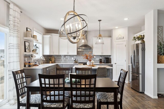 kitchen with wall chimney range hood, light countertops, decorative backsplash, stainless steel fridge, and a sink