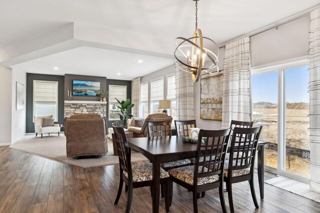 dining space featuring wood finished floors, recessed lighting, an inviting chandelier, a fireplace, and baseboards