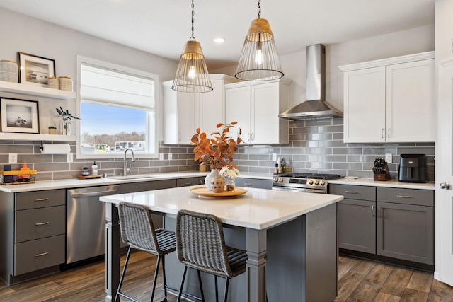 kitchen with wall chimney range hood, gray cabinetry, appliances with stainless steel finishes, and a sink