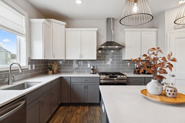 kitchen featuring a sink, wall chimney range hood, appliances with stainless steel finishes, light countertops, and decorative backsplash