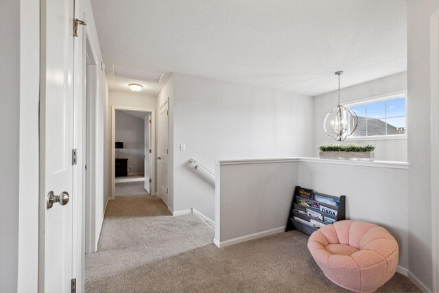 hall with a notable chandelier, an upstairs landing, baseboards, and carpet floors
