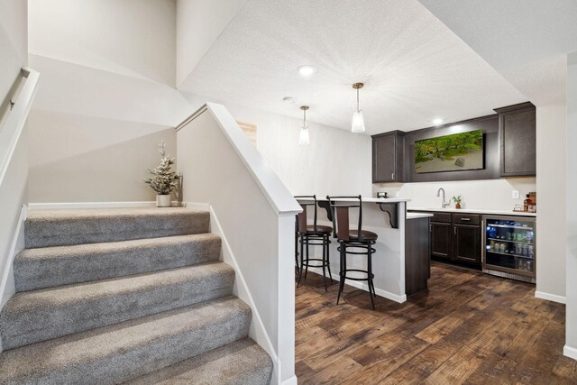 staircase with wood finished floors, beverage cooler, baseboards, wet bar, and a textured ceiling